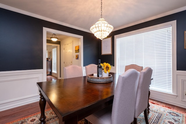 dining space with hardwood / wood-style flooring, crown molding, and an inviting chandelier