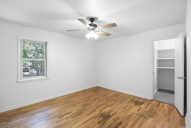 unfurnished bedroom with baseboards, light wood-style flooring, ceiling fan, a spacious closet, and a closet