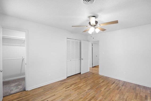 unfurnished bedroom with a textured ceiling, visible vents, baseboards, multiple closets, and light wood-style floors