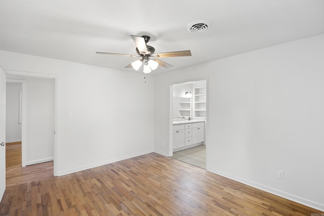 empty room featuring light wood-style flooring, a ceiling fan, visible vents, and baseboards