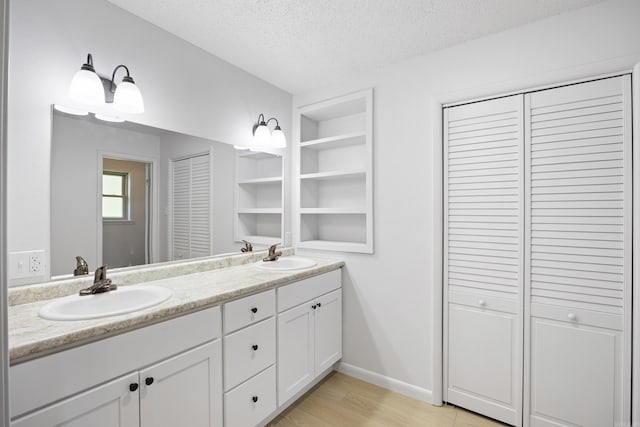 full bathroom with a textured ceiling, double vanity, a closet, and a sink