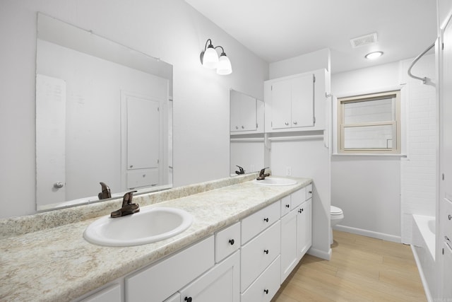 bathroom featuring double vanity, wood finished floors, a sink, and toilet