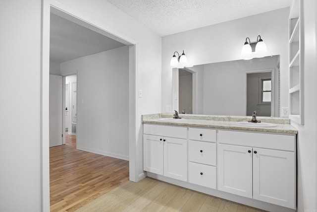 bathroom with double vanity, a textured ceiling, a sink, and wood finished floors