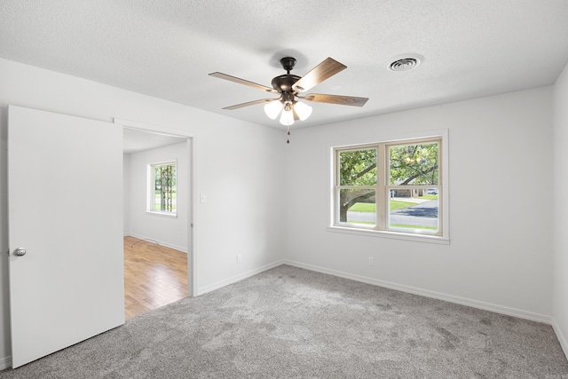 carpeted spare room featuring a textured ceiling, baseboards, visible vents, and a ceiling fan