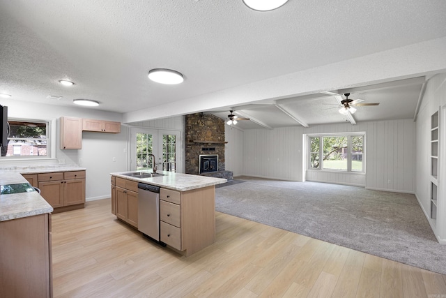 kitchen with a fireplace, light countertops, stainless steel dishwasher, open floor plan, and a sink