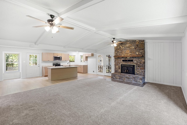 unfurnished living room featuring a ceiling fan, light colored carpet, vaulted ceiling with beams, a stone fireplace, and a sink