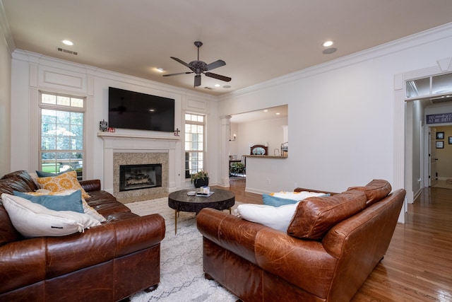 living room with ceiling fan, a tiled fireplace, ornamental molding, and light hardwood / wood-style floors