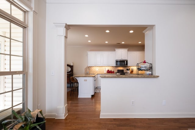 kitchen with kitchen peninsula, backsplash, plenty of natural light, and white cabinetry