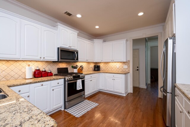 kitchen featuring hardwood / wood-style floors, white cabinetry, appliances with stainless steel finishes, crown molding, and backsplash