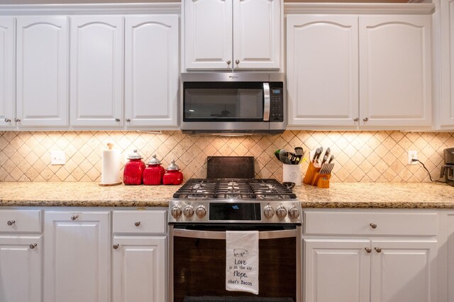 kitchen with decorative backsplash, appliances with stainless steel finishes, light stone counters, and white cabinetry