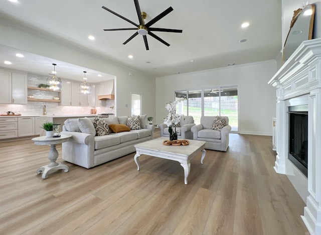 living room with crown molding, ceiling fan, sink, and light wood-type flooring