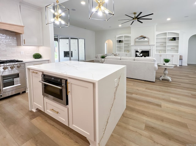 kitchen featuring light stone counters, a center island, appliances with stainless steel finishes, pendant lighting, and white cabinets