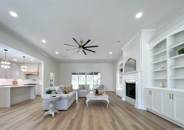 living room with crown molding, ceiling fan with notable chandelier, and light hardwood / wood-style flooring