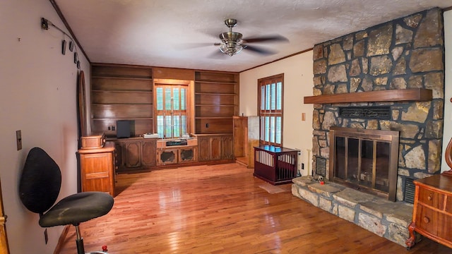 living room with a fireplace, ceiling fan, light hardwood / wood-style floors, crown molding, and a textured ceiling