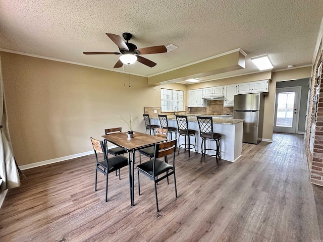 dining room with ceiling fan, a textured ceiling, ornamental molding, and wood-type flooring