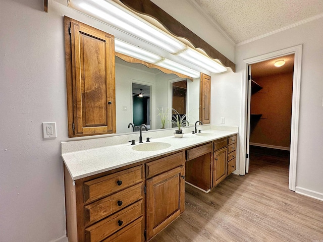 bathroom with dual bowl vanity, a textured ceiling, hardwood / wood-style floors, and crown molding