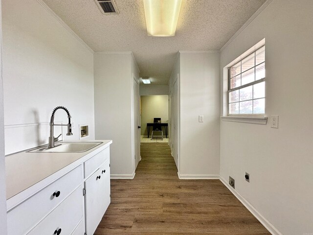 interior space featuring hookup for a washing machine, a textured ceiling, cabinets, sink, and light hardwood / wood-style flooring