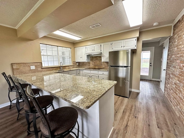 kitchen featuring light hardwood / wood-style flooring, a textured ceiling, white cabinets, stainless steel fridge, and tasteful backsplash