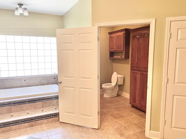 bathroom with a relaxing tiled tub, toilet, and tile patterned flooring