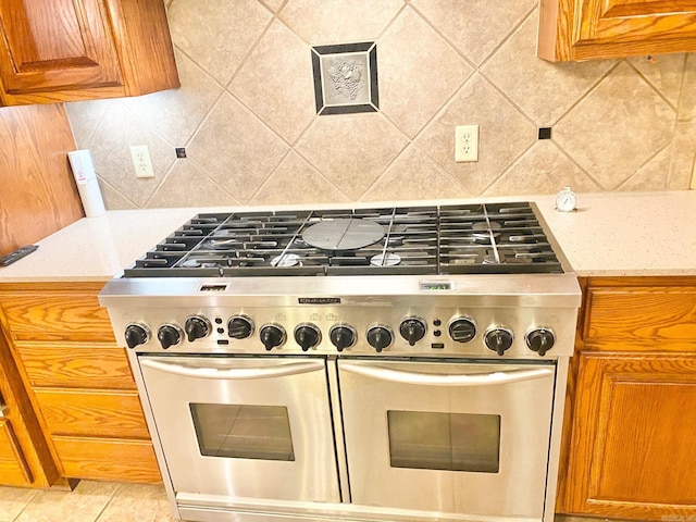 kitchen with light stone countertops, light tile patterned flooring, tasteful backsplash, and range with two ovens