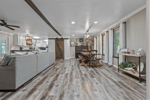 living room with a wealth of natural light, a barn door, ceiling fan, and light hardwood / wood-style floors