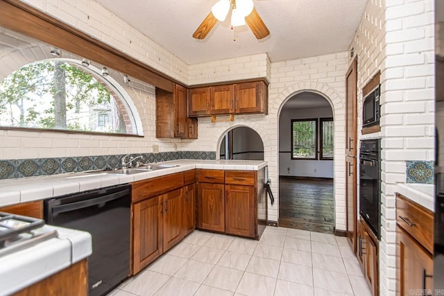 kitchen featuring tile countertops, black appliances, a sink, and brown cabinets