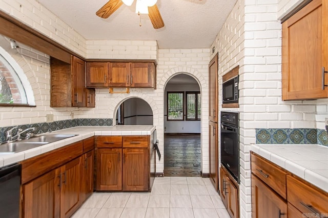 kitchen with black appliances, tile counters, brown cabinetry, and a sink