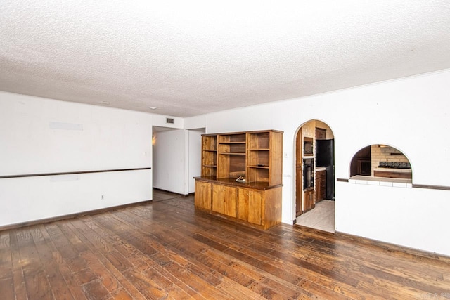 interior space featuring arched walkways, a textured ceiling, visible vents, baseboards, and dark wood finished floors