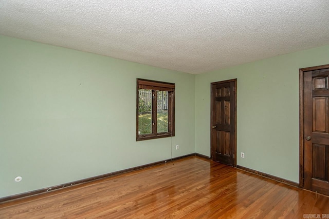 empty room with a textured ceiling, baseboards, and wood finished floors