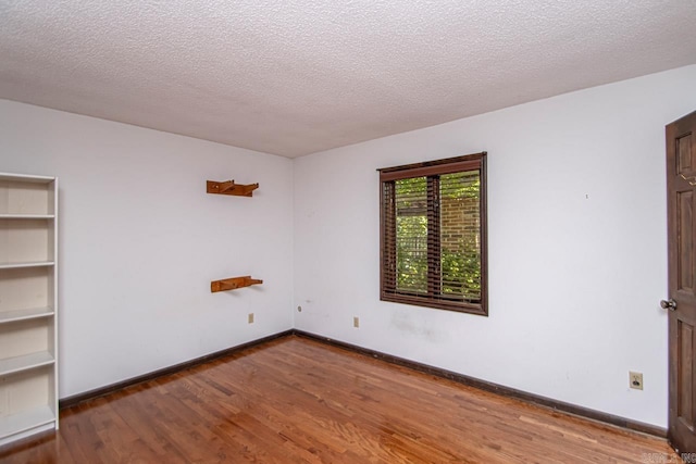 empty room with a textured ceiling, baseboards, and wood finished floors