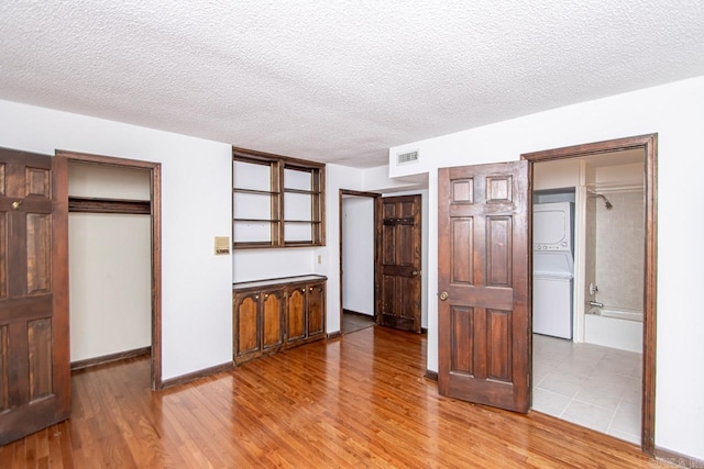 unfurnished bedroom with stacked washer and clothes dryer, a textured ceiling, and wood finished floors