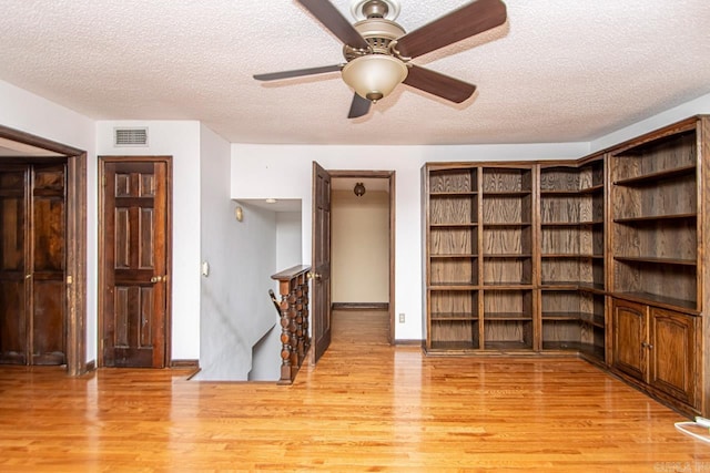 unfurnished room with a textured ceiling, light wood-style flooring, visible vents, baseboards, and a ceiling fan