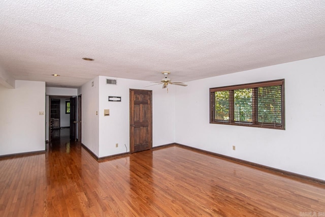 empty room featuring a textured ceiling, ceiling fan, wood finished floors, visible vents, and baseboards