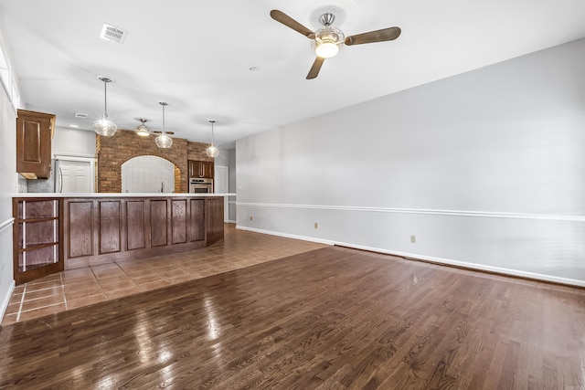 unfurnished living room with ceiling fan, visible vents, and dark wood finished floors