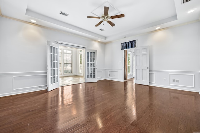 unfurnished room with dark wood-type flooring, a tray ceiling, a healthy amount of sunlight, and visible vents