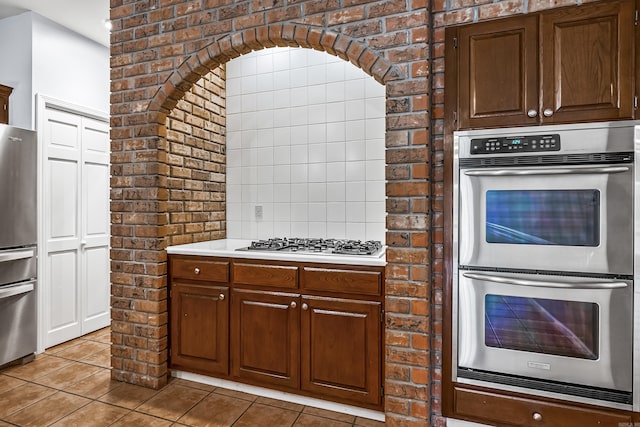 kitchen featuring stainless steel appliances, light countertops, brick wall, and light tile patterned floors