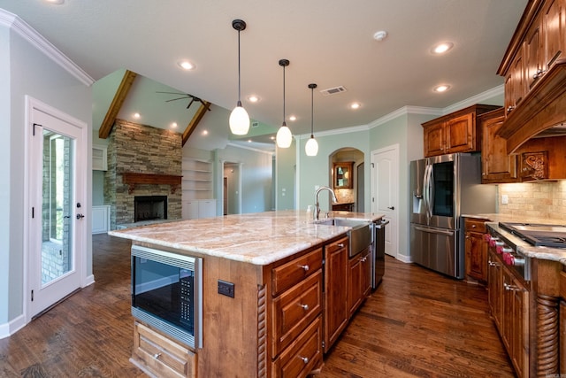 kitchen featuring a spacious island, a stone fireplace, sink, decorative light fixtures, and appliances with stainless steel finishes