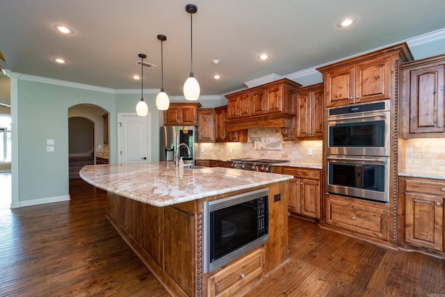 kitchen with dark hardwood / wood-style floors, pendant lighting, a kitchen island with sink, light stone counters, and stainless steel appliances