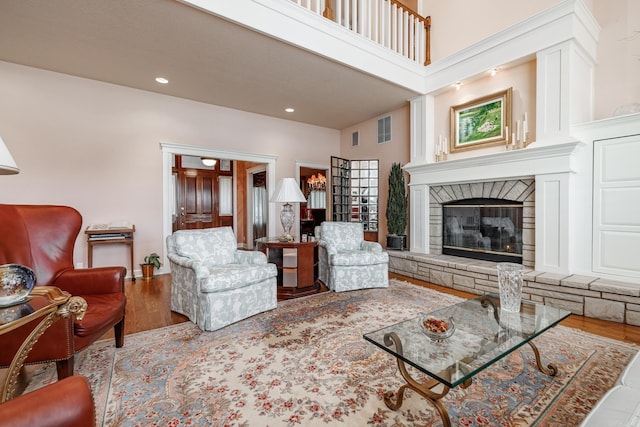 living room with wood-type flooring, a stone fireplace, and a towering ceiling