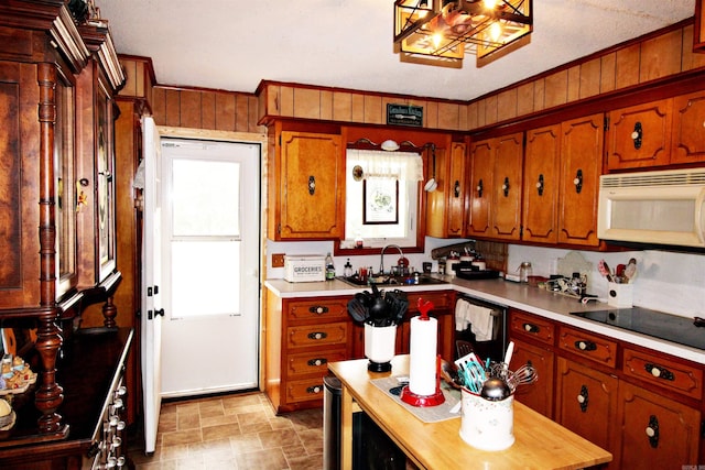 kitchen featuring dishwasher, black electric cooktop, light tile patterned floors, sink, and wood walls