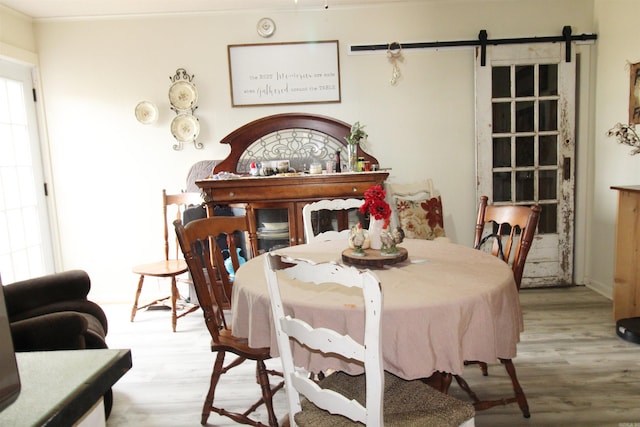 dining room with a barn door, ornamental molding, and hardwood / wood-style flooring