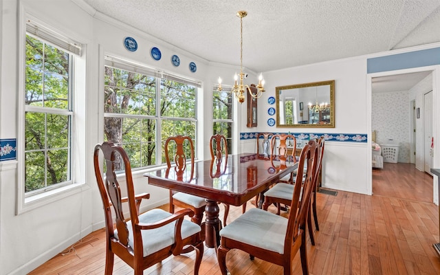 dining room with ornamental molding, a textured ceiling, an inviting chandelier, and light hardwood / wood-style flooring