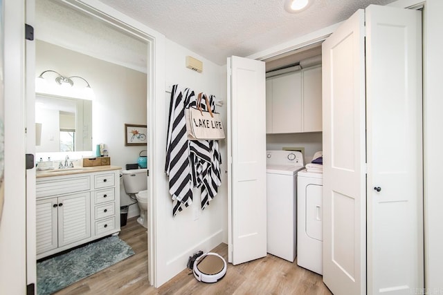 washroom featuring cabinets, a textured ceiling, separate washer and dryer, and light hardwood / wood-style floors