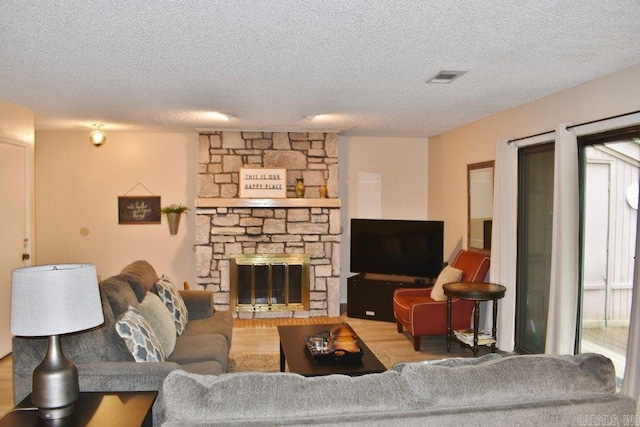 living room featuring light hardwood / wood-style flooring, a textured ceiling, and a stone fireplace