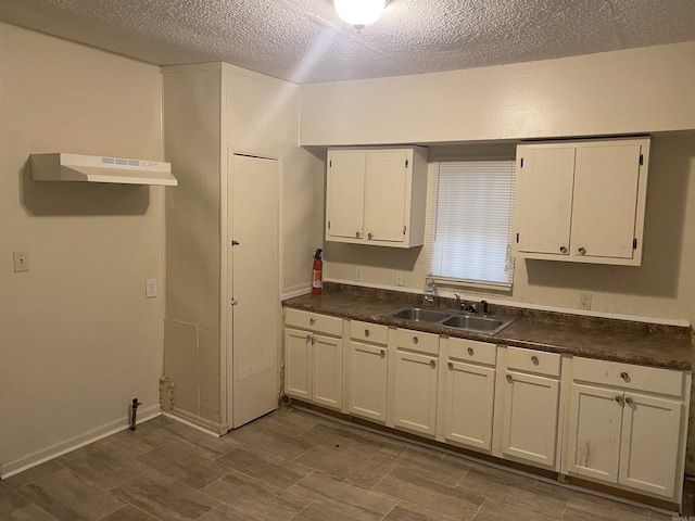 kitchen featuring dark countertops, white cabinetry, a sink, a textured ceiling, and under cabinet range hood