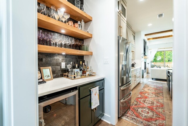 bar featuring wine cooler, light wood-type flooring, tasteful backsplash, and stainless steel refrigerator with ice dispenser