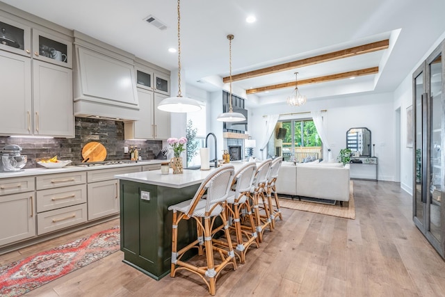 kitchen with gray cabinets, tasteful backsplash, a center island with sink, decorative light fixtures, and light wood-type flooring