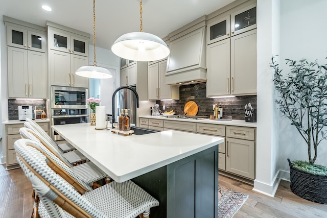 kitchen featuring premium range hood, appliances with stainless steel finishes, pendant lighting, sink, and a kitchen island with sink