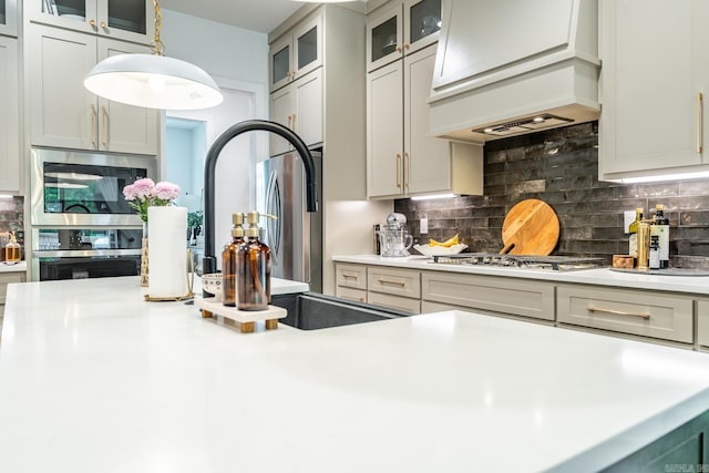 kitchen featuring pendant lighting, decorative backsplash, appliances with stainless steel finishes, and custom range hood