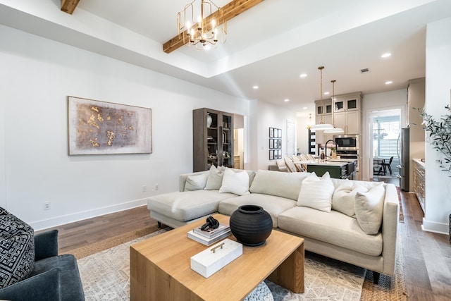 living room featuring wood-type flooring, beam ceiling, a chandelier, and sink